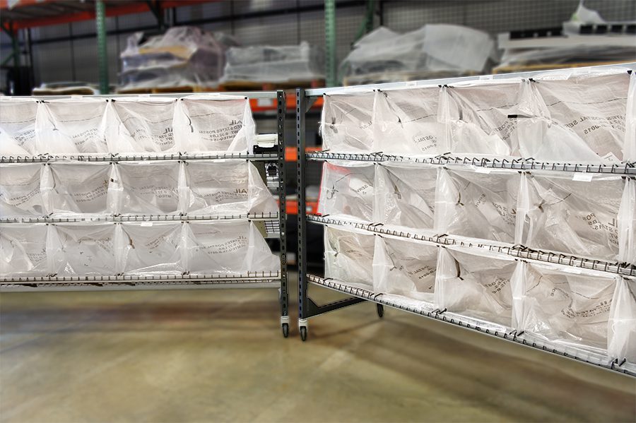 The LightSort Bag Rack with Sort-to-Light and attached U.S.P.S. Mail bags attached sits in a warehouse with a blurry background