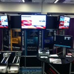Engineering Innovation's booth with several machines, posters, and tv monitors playing videos at the 2011 Modex trade show.