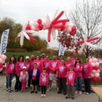 Group of Engineering Innovation employees wearing pink shirts and standing underneath a pink balloon arch.