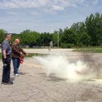 Customer support technician, Issac Smith, practices using a fire extinguisher in a parking lot as part of emergency fire safety training.