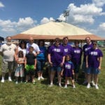 Group of Engineering Innovation employees wearing purple shirts and standing in a grassy field at the 2016 Relay for Life.