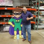 Engineering Innovation employee poses for a photo with a large cardboard cut out of a super hero.