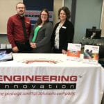 Three Engineering Innovation employees stand behind a table with product brochures at the Ivy Tech job fair.