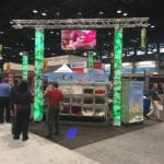 Engineering Innovation's picnic themed booth with large, green-lit trusses, ivy, and several mail sorting machines.