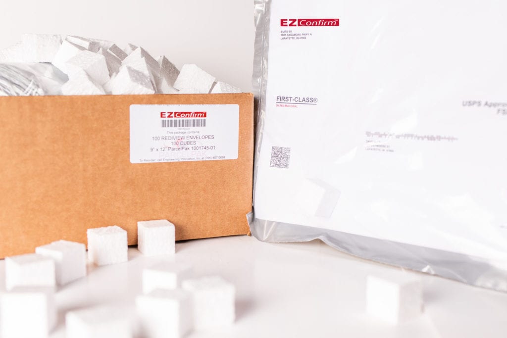 A cardboard box filled with small, white, Styrofoam cubes and a large, white first-class envelope both labeled with an "EZ-Confirm" logo.