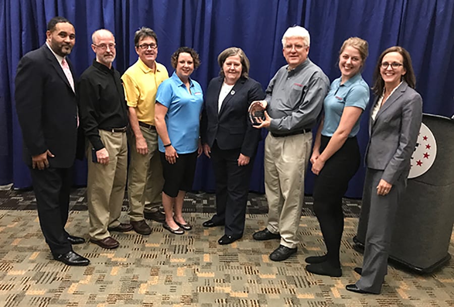 A group of Engineering Innovation employees poses for a photo with the Postmaster General while accepting the 2017 USPS award.