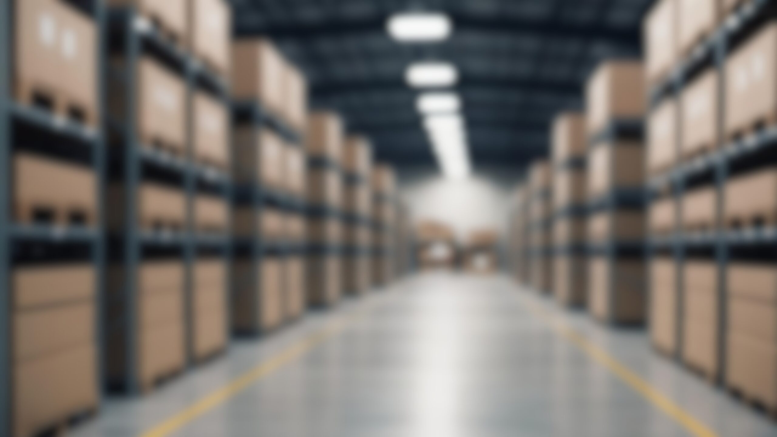 Blurred image of a warehouse with rows of shelves stacked with cardboard boxes. The floor is smooth, and lights illuminate the space from above, creating a vanishing point perspective down the aisle.