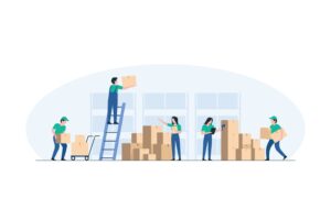 Five people in green shirts efficiently organize and move boxes in a warehouse. Using a sorting system, one stands on a ladder, while others carry boxes, use a hand truck, and check a clipboard near shelves stacked with cartons.