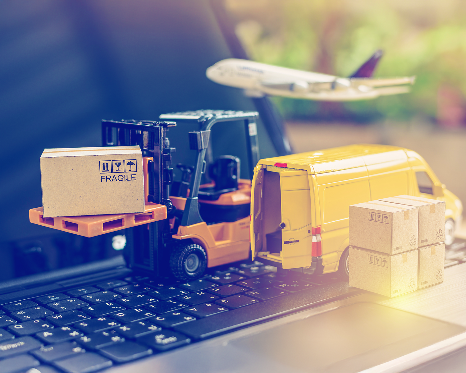 Toy models of a forklift, delivery van, and airplane with cardboard boxes are placed on a laptop keyboard, symbolizing global logistics and online shipping services.