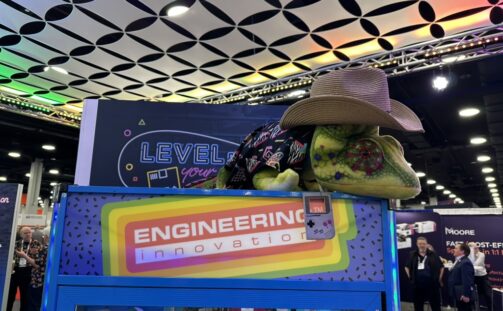 A large chameleon statue wearing a cowboy hat and jacket sits atop a colorful 