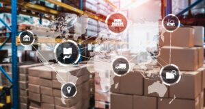 Stacks of cardboard boxes in a warehouse with a transparent world map overlay showing interconnected supply chain icons, including trucks, warehouses, shipping, and inventory management symbols.