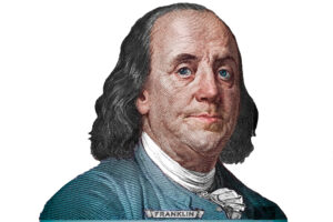 Engraved illustration of Benjamin Franklin with shoulder-length hair, wearing a blue coat, white shirt, and a cravat; the name “Franklin” appears on his collar. The image has a white background.