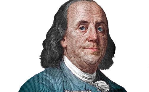 Engraved illustration of Benjamin Franklin with shoulder-length hair, wearing a blue coat, white shirt, and a cravat; the name “Franklin” appears on his collar. The image has a white background.