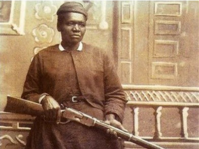 A Black woman in historical clothing sits on a bench, holding a long rifle across her lap. The sepia-toned image, evoking postal history, features a decorative background with intricate patterns and wooden door panels.